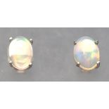 A white metal pair of single stone stud earrings. Each set with an oval cabochon cut welo opal.