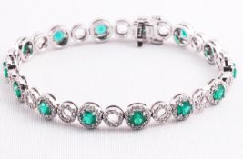 A white metal bracelet set with fourteen round faceted cut emeralds and finished with round