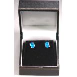 A white metal pair of single stone stud earrings. Each set with an oval cut intense blue apatite.