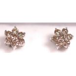 A white metal pair of floral cluster studs. Each set with seven round brilliant cut diamonds.