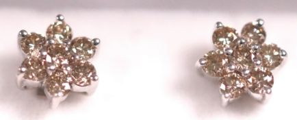 A white metal pair of floral cluster studs. Each set with seven round brilliant cut diamonds.