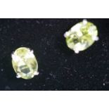 A white metal pair of single stone stud earrings. Each set with an oval faceted cut peridot.