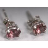 A white metal pair of single stone stud earrings. Each set with an oval cut pink tourmaline.