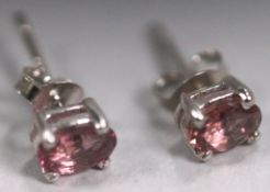A white metal pair of single stone stud earrings. Each set with an oval cut pink tourmaline.