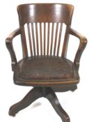 An oak office leather chair, with arms, swivelling on four splayed legs each with casters,