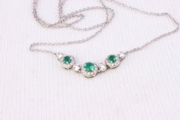 A white metal necklace having a centrepiece design and set with emeralds and diamonds.