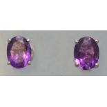 A white metal pair of single stone stud earrings, each set with an oval faceted cut amethyst.