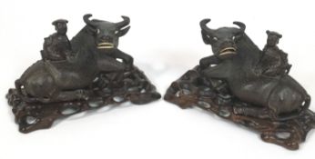 A pair of Chinese carved wood sculptures of water buffalo with a seated figure on their backs,