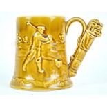 A pottery tankard, moulded with a golfing scene, the handle in the form of a bag of golf clubs,