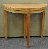 A light wood demi-lune table on three legs,