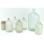 A collection of five demi johns, a stoneware storage jar and a large demi john,