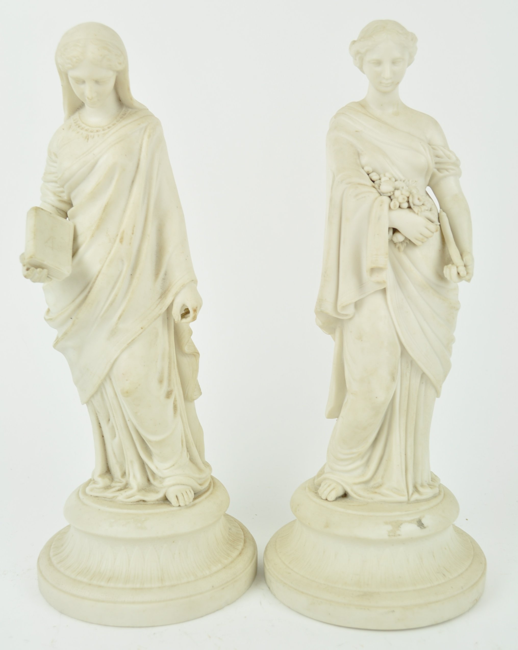 A pair of Parian figures of maidens in draped dresses, one holding a book,