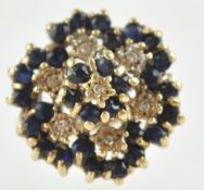 A yellow metal large cluster ring. Set with dark blue faceted cut sapphires and single cut diamonds.