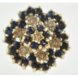 A yellow metal large cluster ring. Set with dark blue faceted cut sapphires and single cut diamonds.