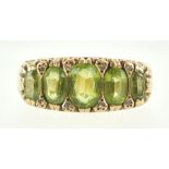 A yellow metal half hoop ring set with five graduated oval faceted cut peridot and interspaced with