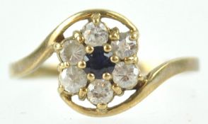 A yellow metal floral crossover ring set with a central sapphire and surrounded by cubic zirconia.