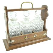 An oak framed tantalus, with brass handle, enclosing three square cut decanters and stoppers,