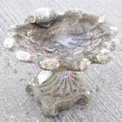 A reconstituted stone bird bath in the form of a shell on four scroll feet,