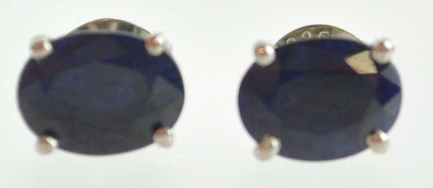 A white metal pair of single stone stud earrings.