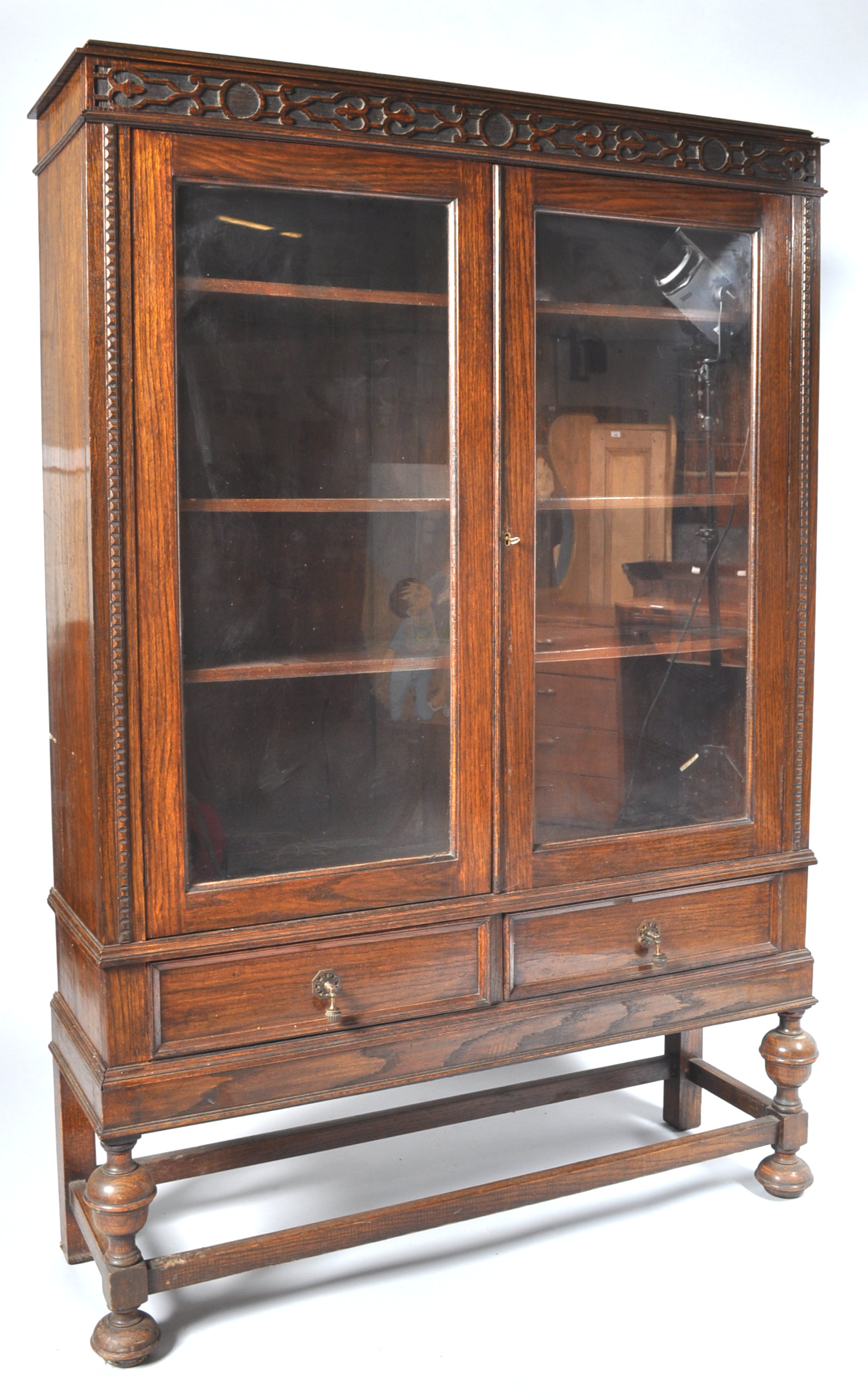 An oak display cabinet with two glazed doors above two frieze drawers on baluster turned legs,