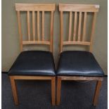 A pair of light wood dining chairs with black seats,