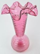 A large cranberry tinted vase with globular body and flared neck, terminating in a wide frill rim,