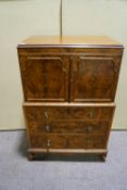 A walnut chest of drawers with two panelled cupboard doors above,