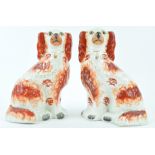 A pair of 19th century Staffordshire pottery figures of spaniels, picked out in iron red enamels,