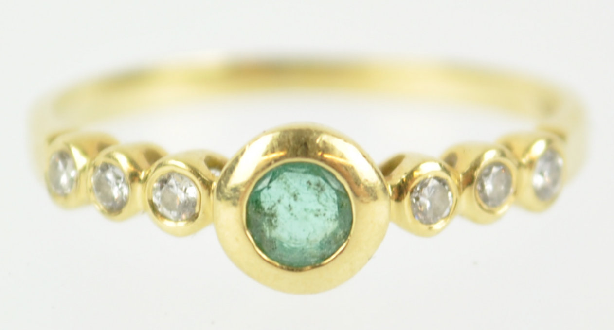 A yellow metal ring principally set with a round cut emerald and flanked by three diamonds to each