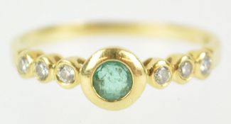 A yellow metal ring principally set with a round cut emerald and flanked by three diamonds to each