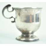A silver miniature mug, of plain bell bowl on a raised foot and with a contrived strap handle,