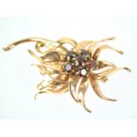 A yellow metal floral spray brooch centrally set with round cut garnets.
