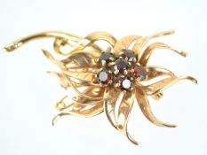 A yellow metal floral spray brooch centrally set with round cut garnets.