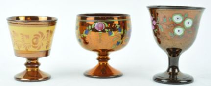 Three mid 19th century copper lustre pottery goblets, two painted with flowers, the largest 10.