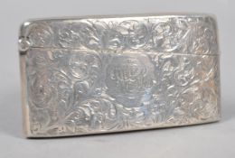 A silver card case of shaped rectangular form, profusely engraved with scrolling foliates