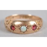 A yellow metal ring principally set with a cabochon cut opal and flanked by two synthetic rubies.