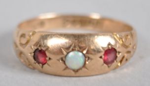 A yellow metal ring principally set with a cabochon cut opal and flanked by two synthetic rubies.