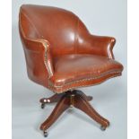A swivel office chair, upholstered in studded tan leather, on four reeded legs and casters,