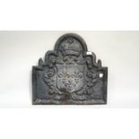 A cast iron fire back of an arched scrolled form decorated with an armorial surmounted by a crown,