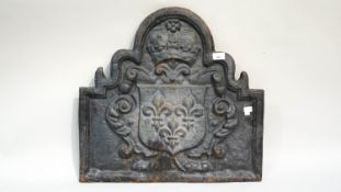 A cast iron fire back of an arched scrolled form decorated with an armorial surmounted by a crown,