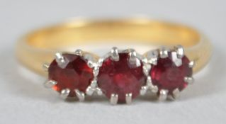 A yellow and white metal ring set with three round faceted cut garnets. No hallmark - stamped 18ct.