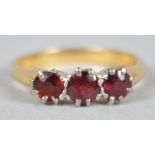 A yellow and white metal ring set with three round faceted cut garnets. No hallmark - stamped 18ct.