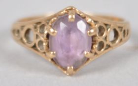 A yellow metal single stone ring. Set with an oval faceted cut pale amethyst.