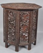 A teak occasional table of octagonal section with chip-carved top with continuous fruiting vine,