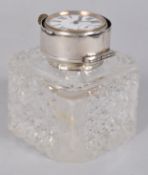 A large cut glass square form inkwell with cut corners, set with a hinged silver cover