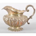 A silver milk jug, with wave style rim over a bellied floral repousse decorated body,