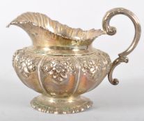 A silver milk jug, with wave style rim over a bellied floral repousse decorated body,