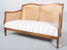 An Edwardian mahogany single cane bergere two seat sofa with caned back and arm and upholstered