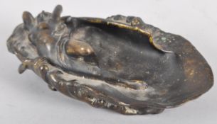 An Art Nouveau bronze sculpture, cast as a scantily draped maiden lying across an oyster shell,