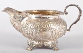 An Irish silver milk jug, of heavily repousse decorated floral scroll round form,